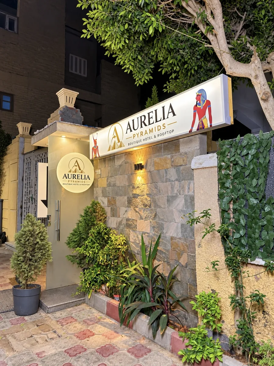 Entrance of Aurelia Pyramids at night with the illuminated sign, the round logo on the glass door and garden plants