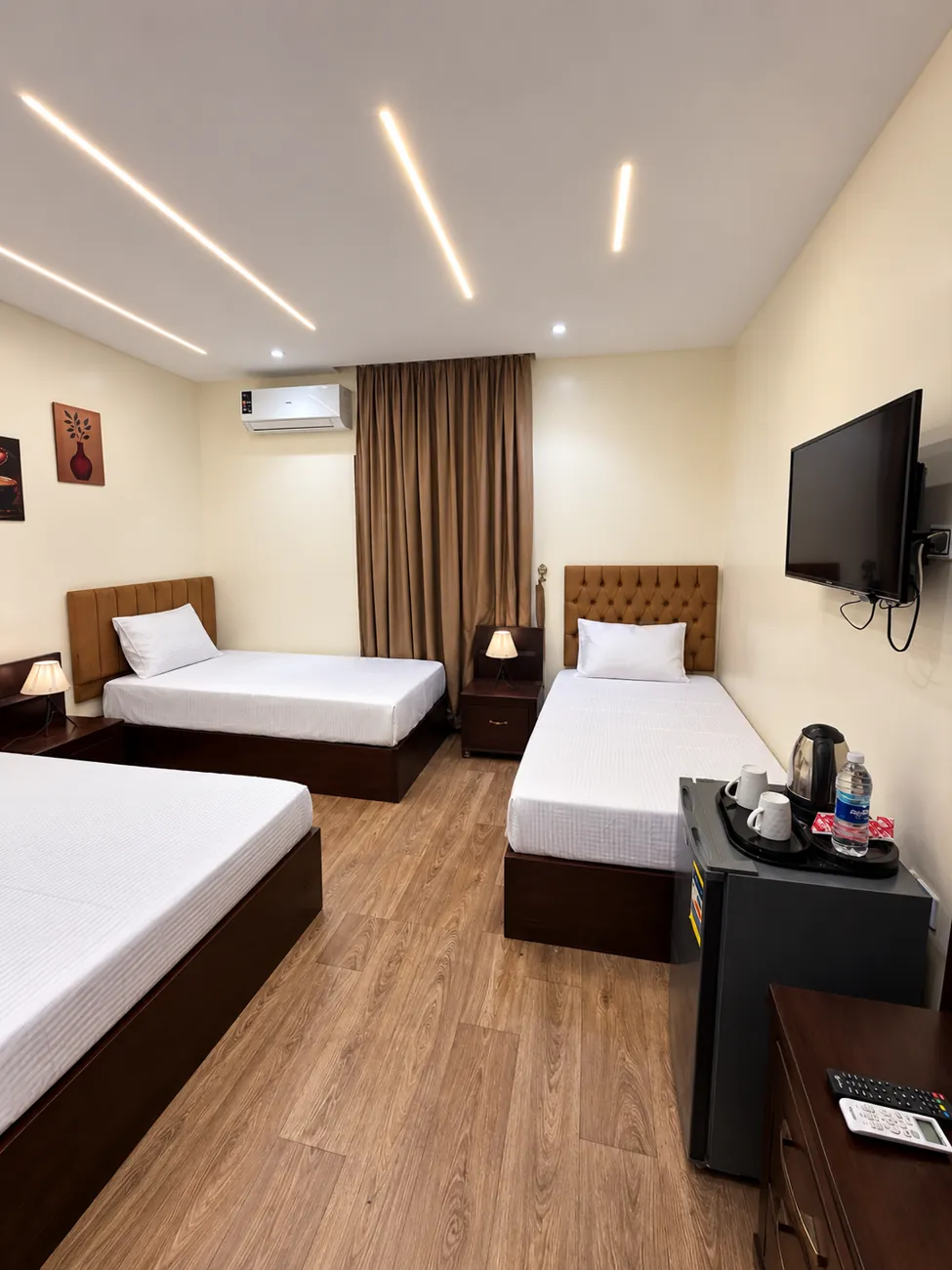Family room 205 with one double bed and two single beds, linear ceiling lights and wall mounted TV